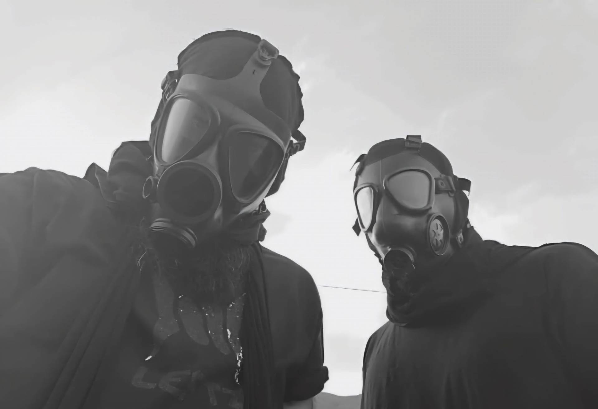 Two members of Wayloun wearing gas masks in a black-and-white photo with a dramatic sky in the background.