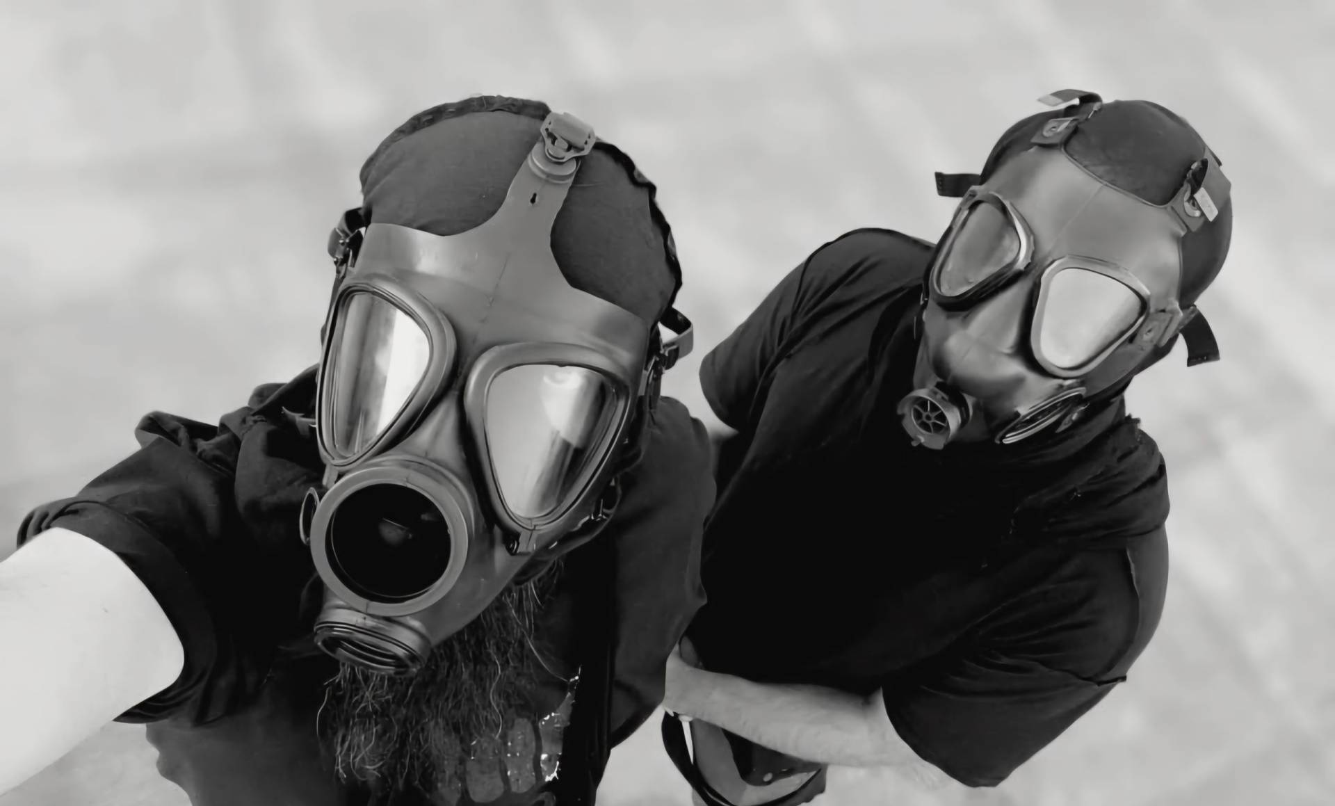Two members of Wayloun wearing gas masks, shot in black and white, looking up at the camera with intense presence.