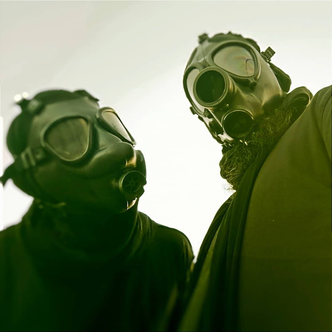 Two members of Wayloun wearing black clothes and gas masks, standing side by side against a pale sky, portraying a dystopian and rebellious aesthetic.